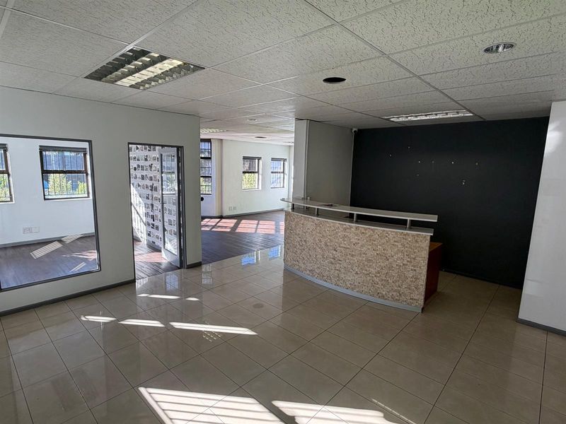 Open-plan office space featuring a built-in reception desk, tiled and laminate flooring, and suspended ceilings with recessed lighting.