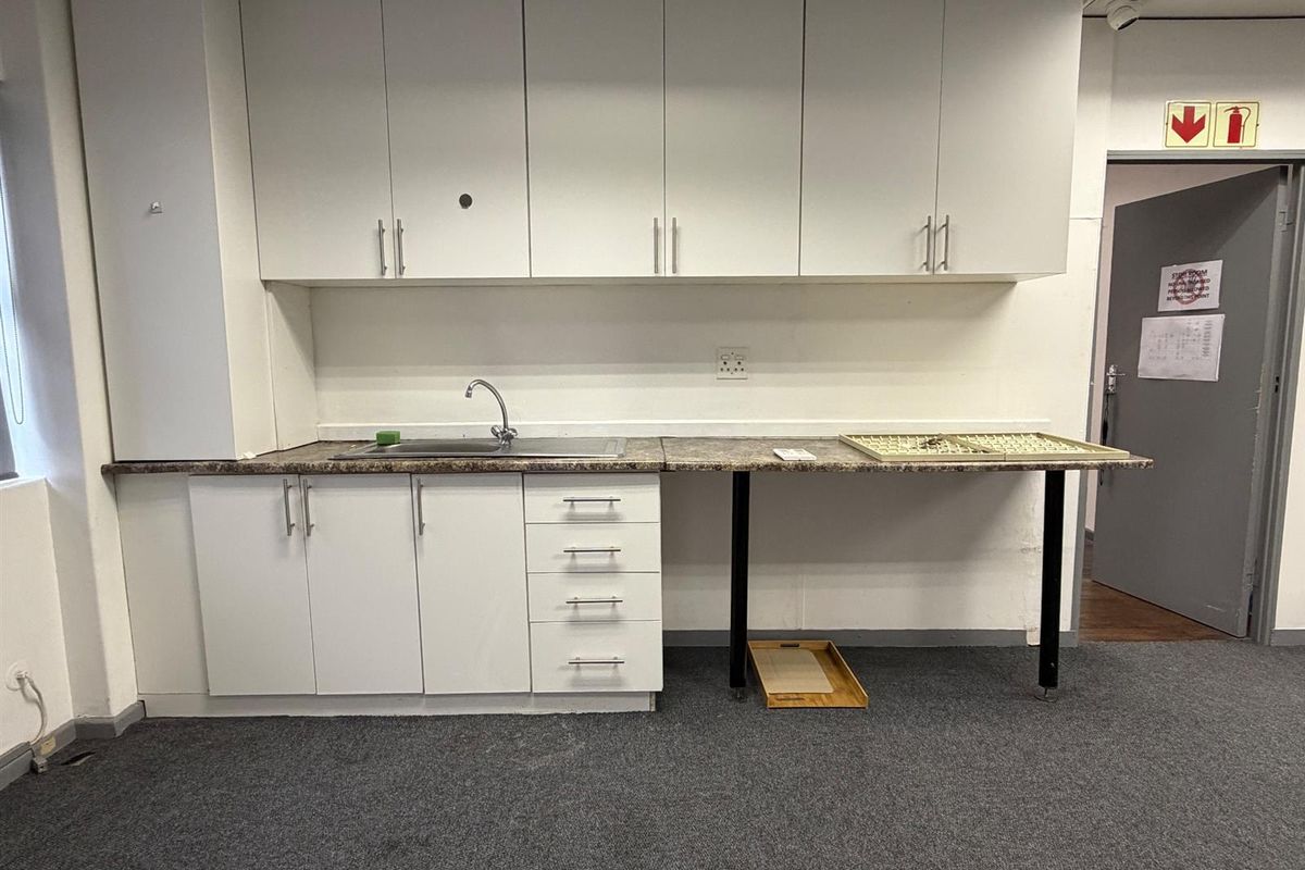 A functional office kitchenette featuring white built-in cabinetry, a stainless steel sink, and a laminate countertop, providing a practical utility space for staff.