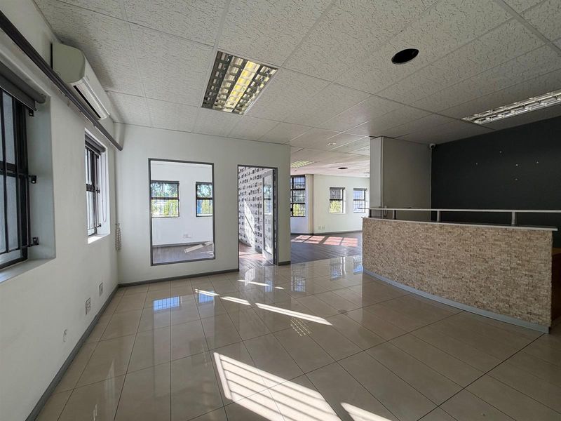 Spacious open-plan office area featuring tiled flooring, a reception counter, drop ceilings with integrated lighting, and split-system air conditioning.