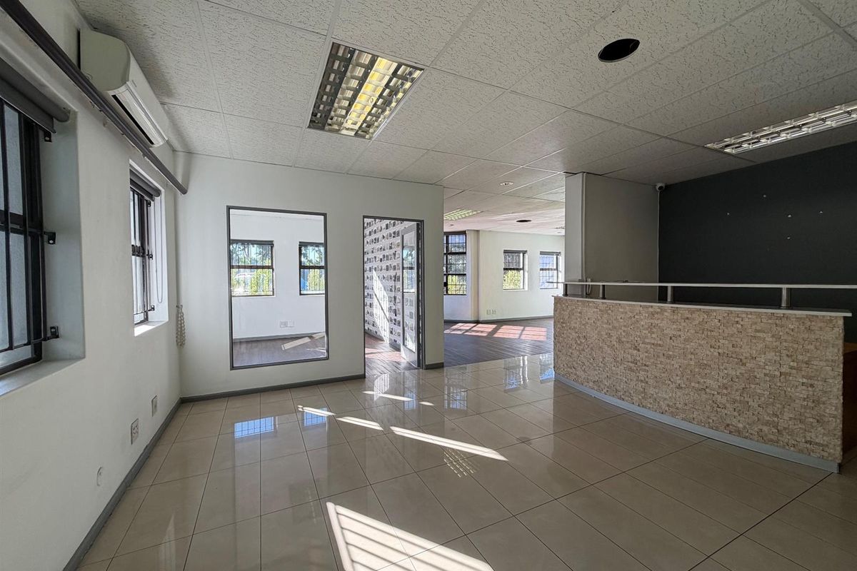 Spacious open-plan office area featuring tiled flooring, a reception counter, drop ceilings with integrated lighting, and split-system air conditioning.