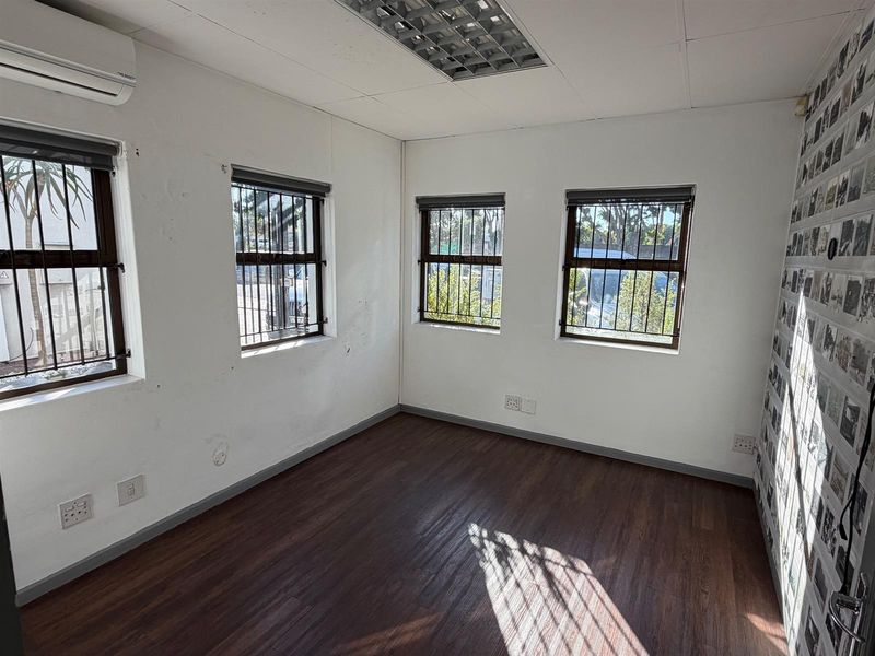 A vacant office space featuring laminate flooring, recessed ceiling lighting, air conditioning, and security bars on the windows.