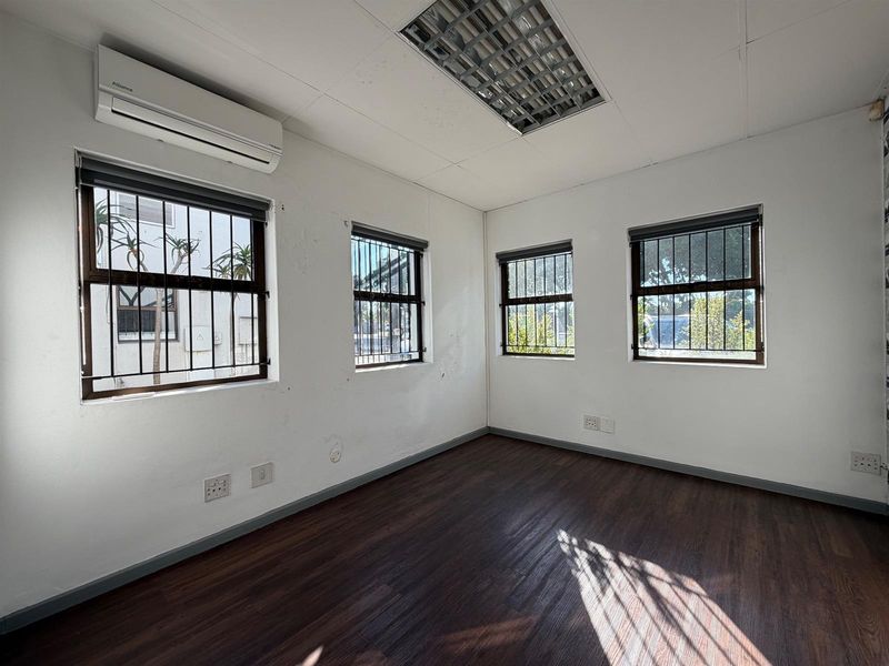 A vacant office space featuring laminate flooring, security bars on windows, a split-system air conditioner, and recessed ceiling lighting.
