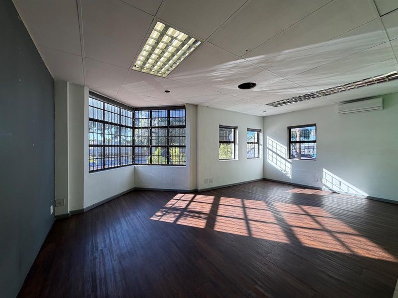 Spacious, empty office area featuring laminate flooring, recessed lighting, split-system air conditioning, and large windows with security bars.