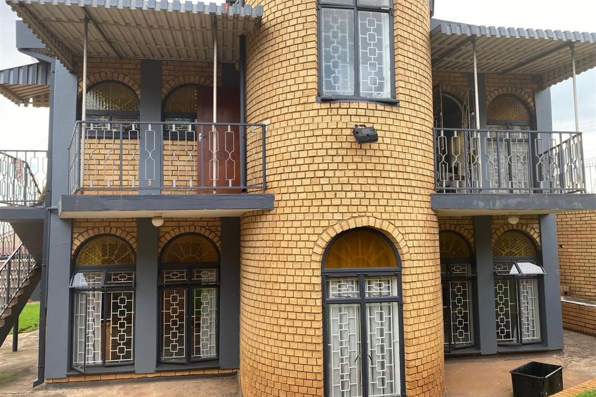 A two-story residential exterior featuring a distinctive circular brick tower design with arched windows, metal security grilles, and covered balconies.