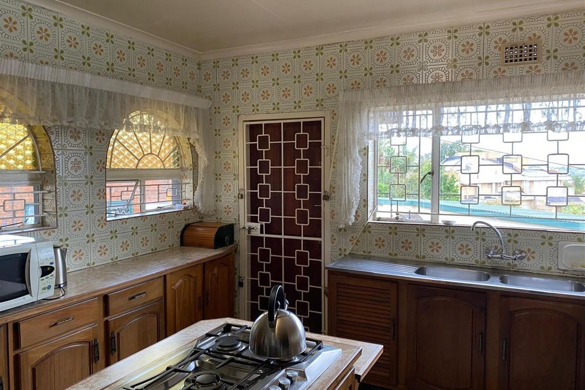 A dated kitchen featuring traditional wooden cabinetry, a central island with a built-in gas hob, and patterned wall tiles.