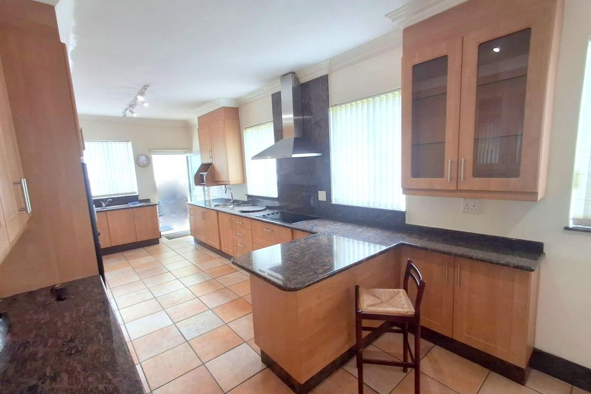 Spacious kitchen featuring light wood cabinetry, dark granite countertops, stainless steel extractor fan, and tiled flooring with a breakfast nook area.