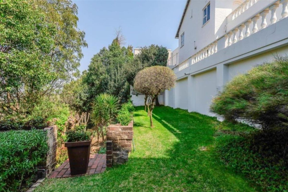A well-maintained rear garden area featuring a lush lawn, established trees, and a brick-paved pathway alongside the side elevation of the house.