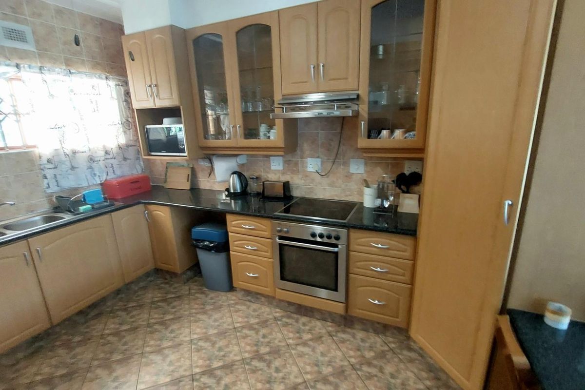A functional kitchen featuring wooden cabinetry, dark granite countertops, a built-in oven, electric hob, and an extractor fan.
