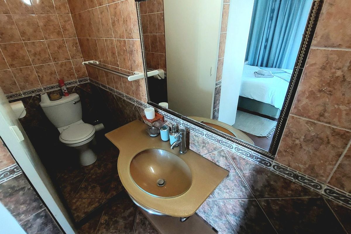 A compact bathroom featuring dated ceramic wall and floor tiles, a wall-mounted vanity with integrated basin, and a standard toilet suite.