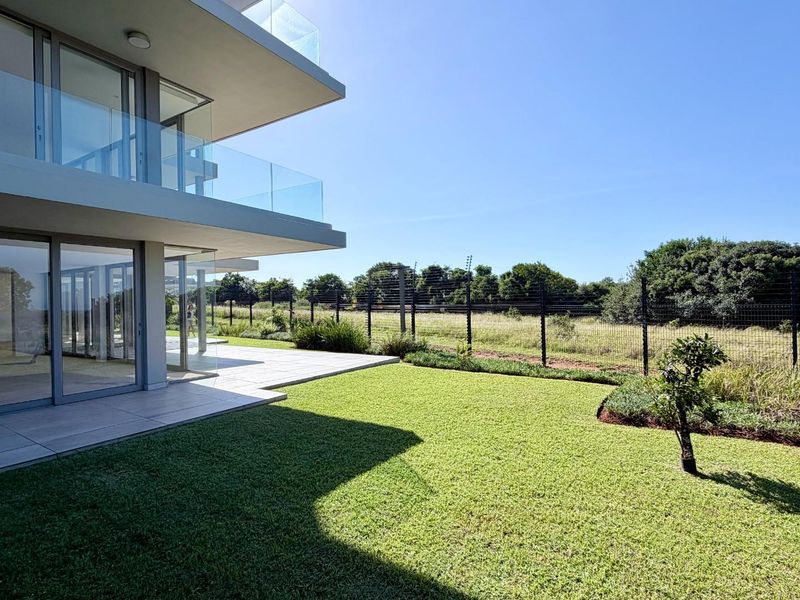 Modern apartment exterior featuring a spacious tiled patio, glass balustrades, and a well-maintained private garden area with secure perimeter fencing.
