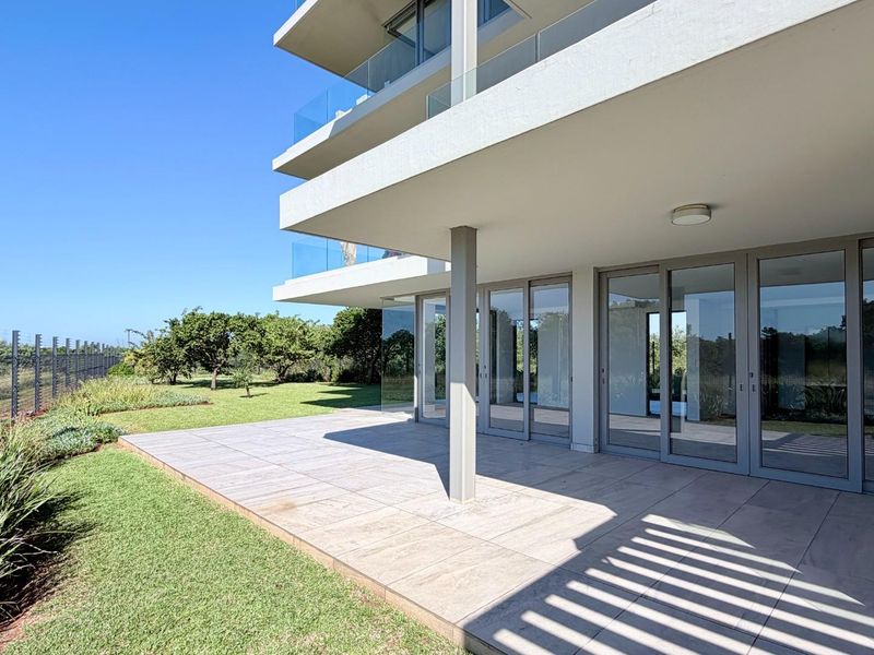 A spacious ground-floor tiled patio featuring modern glass sliding doors, glass balustrades, and direct access to a well-maintained garden area.