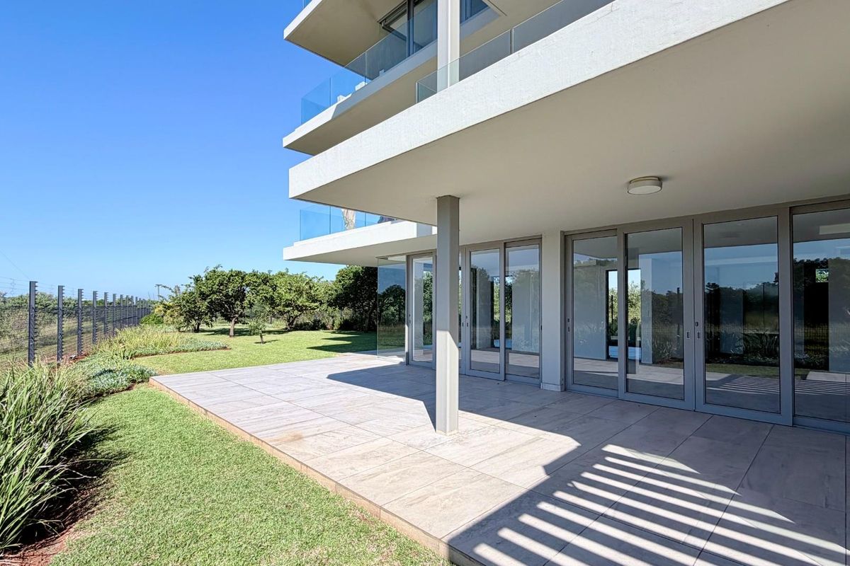 A spacious ground-floor tiled patio featuring modern glass sliding doors, glass balustrades, and direct access to a well-maintained garden area.