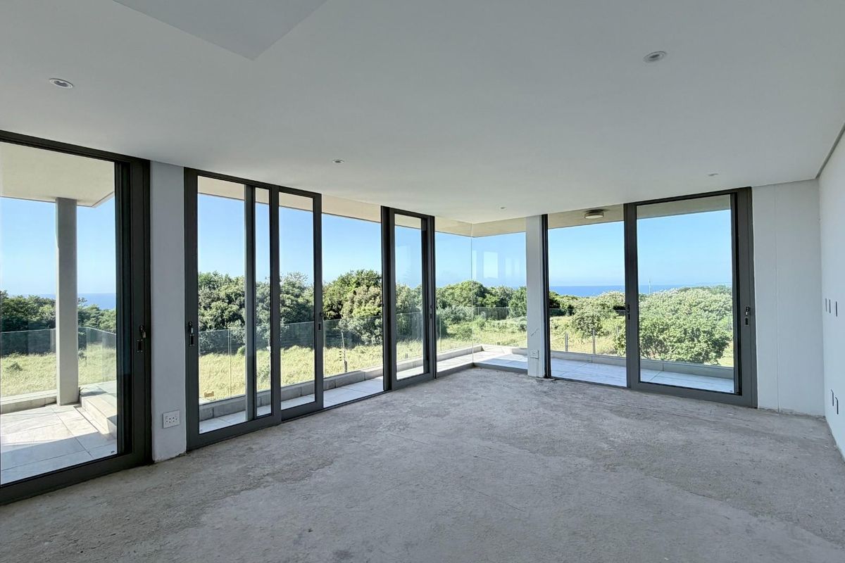 Spacious, light-filled living area featuring expansive floor-to-ceiling sliding glass doors that open onto a balcony with scenic coastal views.
