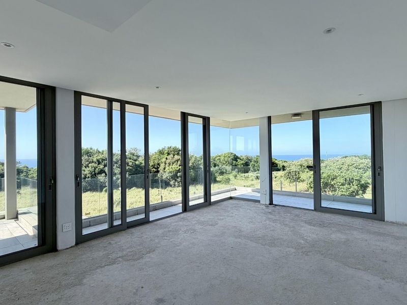 Spacious, light-filled living area featuring expansive floor-to-ceiling sliding glass doors that open onto a balcony with scenic coastal views.