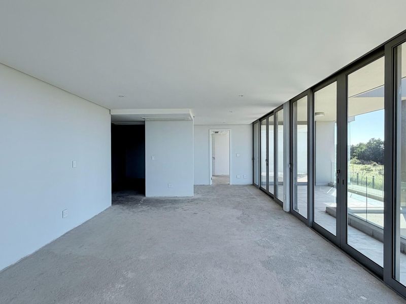 Spacious, empty living area featuring floor-to-ceiling glass sliding doors that open onto a balcony with a glass balustrade.