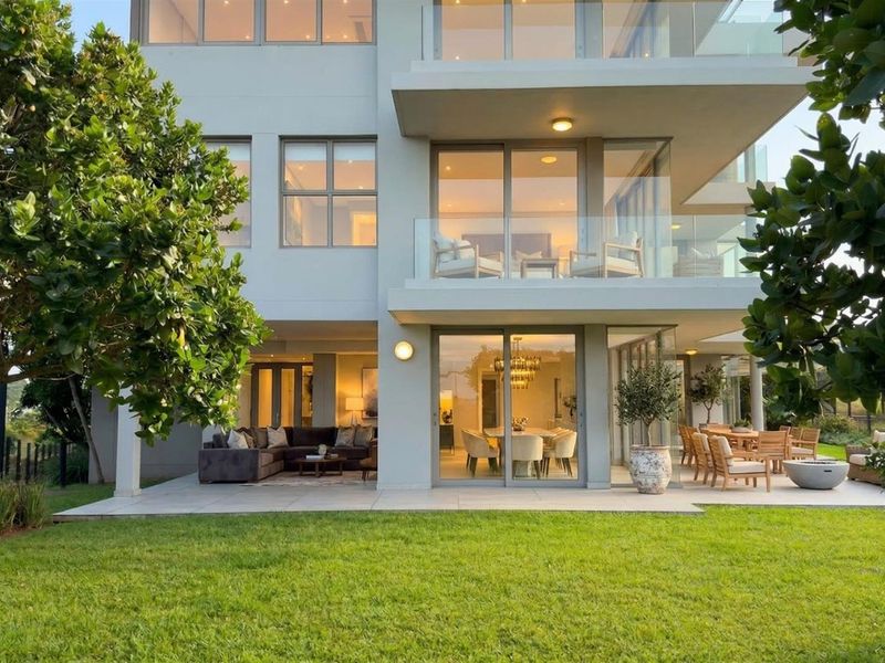 Rear view of a modern multi-story apartment building featuring a spacious tiled patio, glass balustrades, and large sliding doors opening to the garden.