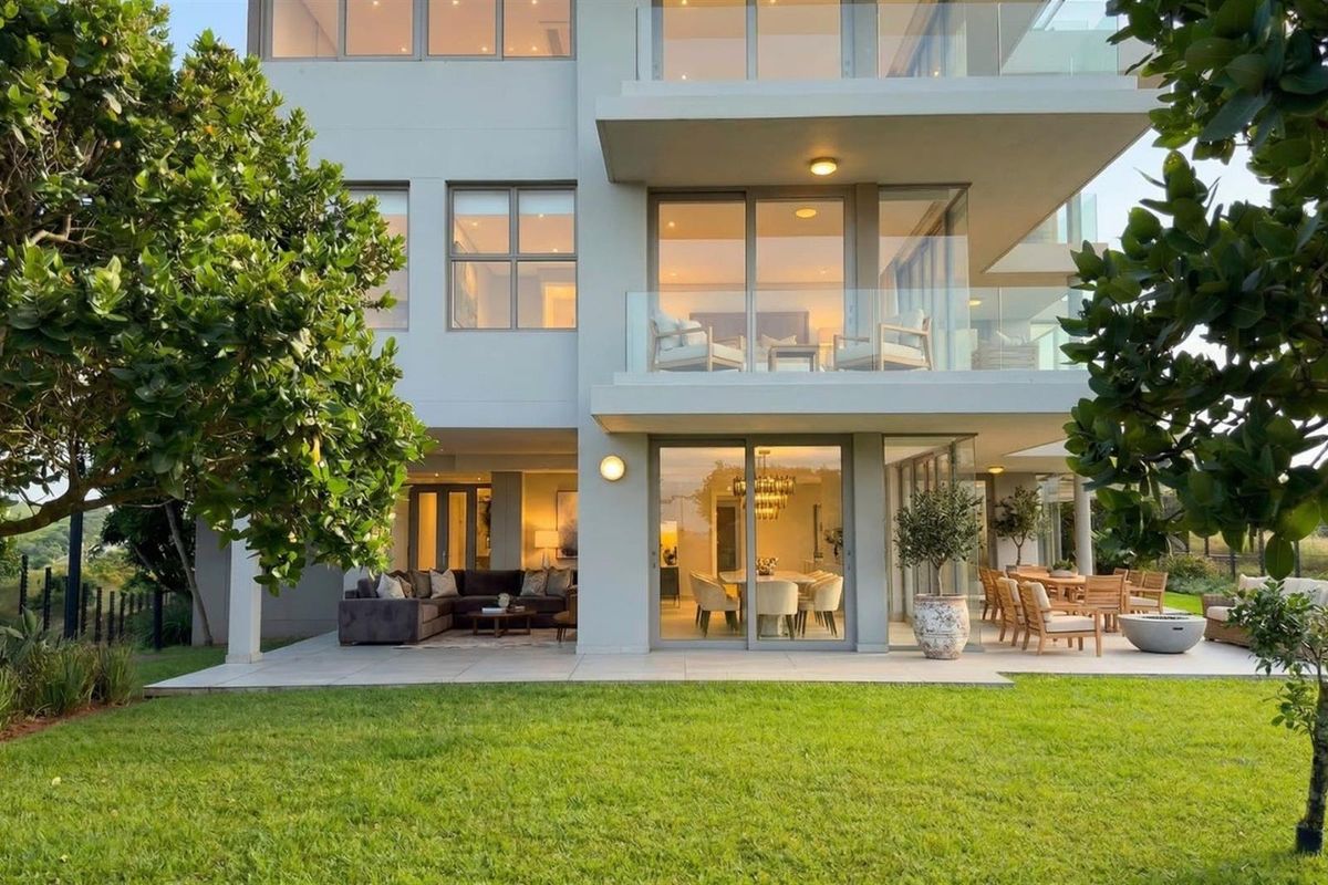 Rear view of a modern multi-story apartment building featuring a spacious tiled patio, glass balustrades, and large sliding doors opening to the garden.