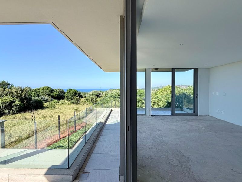 Spacious open-plan living area featuring large sliding glass doors that open onto a balcony with scenic views and a modern glass balustrade.