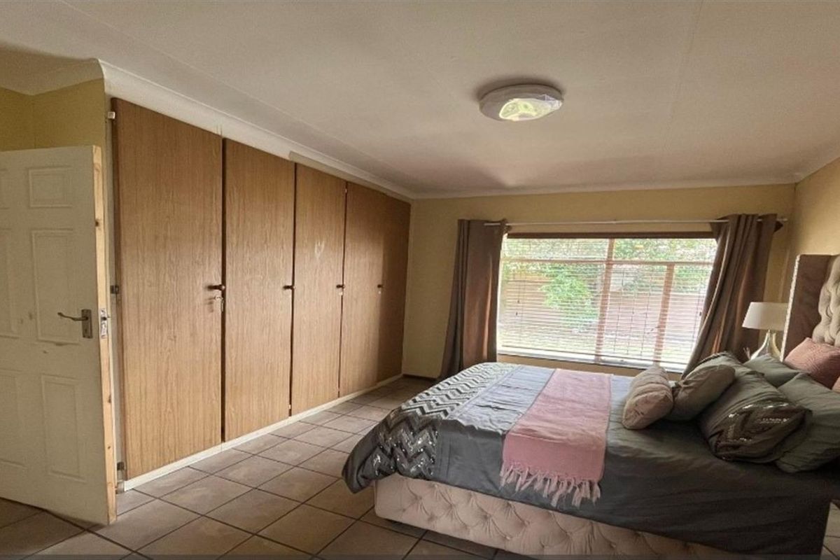A bedroom featuring built-in wooden cupboards, tiled flooring, and a large window providing natural light.