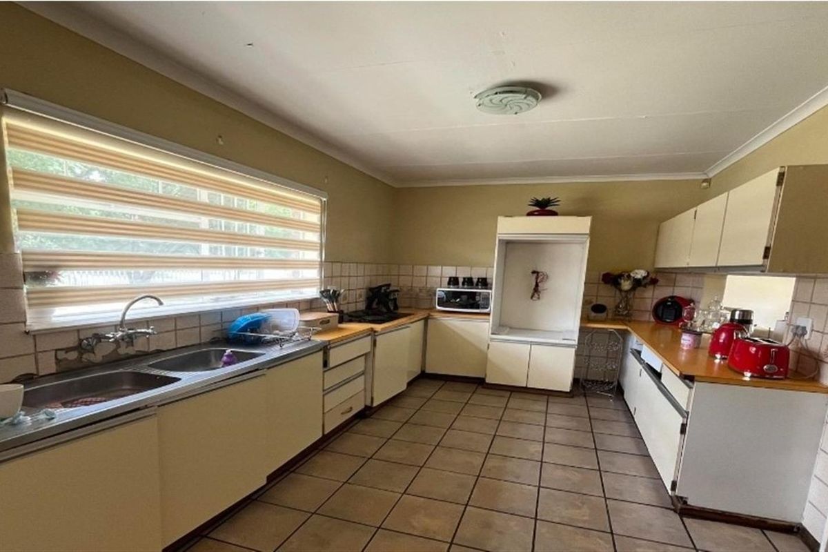 A functional kitchen featuring laminate countertops, tiled backsplash, double stainless steel sink, and ample built-in cabinetry with a dedicated appliance housing unit.