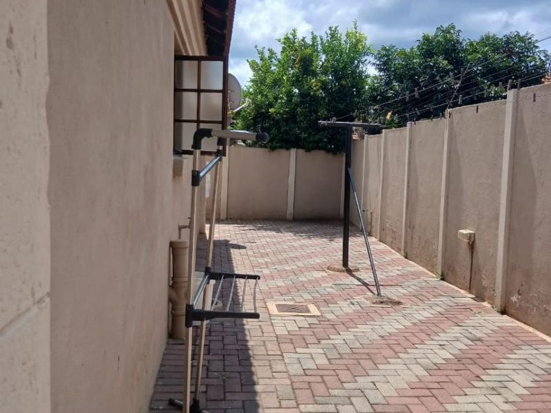 A paved side yard area featuring a boundary wall with security fencing and external plumbing fixtures.