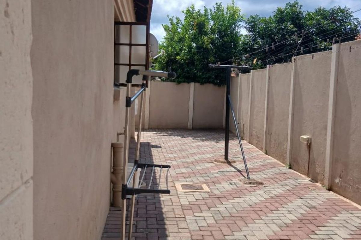 A paved side yard area featuring a boundary wall with security fencing and external plumbing fixtures.