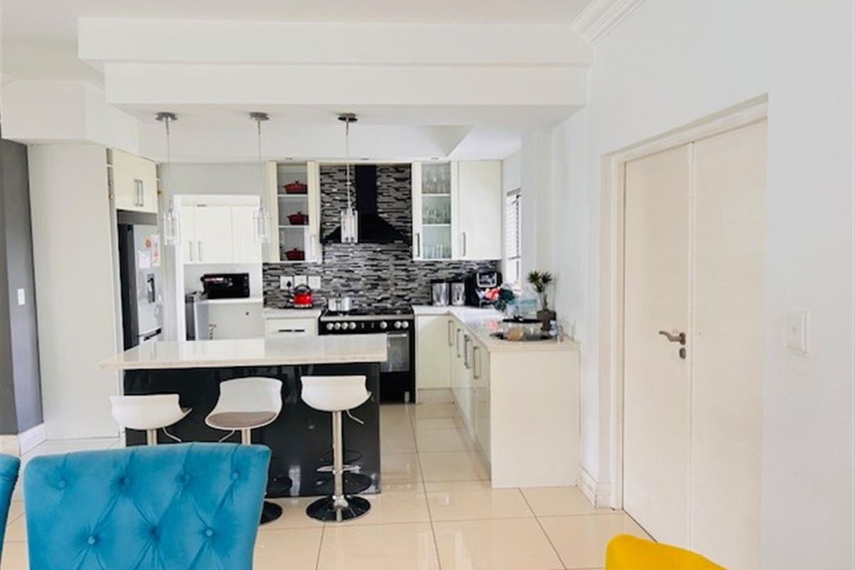 Modern kitchen featuring a central island with stone countertops, sleek cabinetry, built-in oven, extractor fan, and polished tiled flooring.