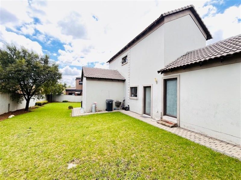 Rear view of the house featuring a well-maintained lawn, paved walkway, and boundary wall.