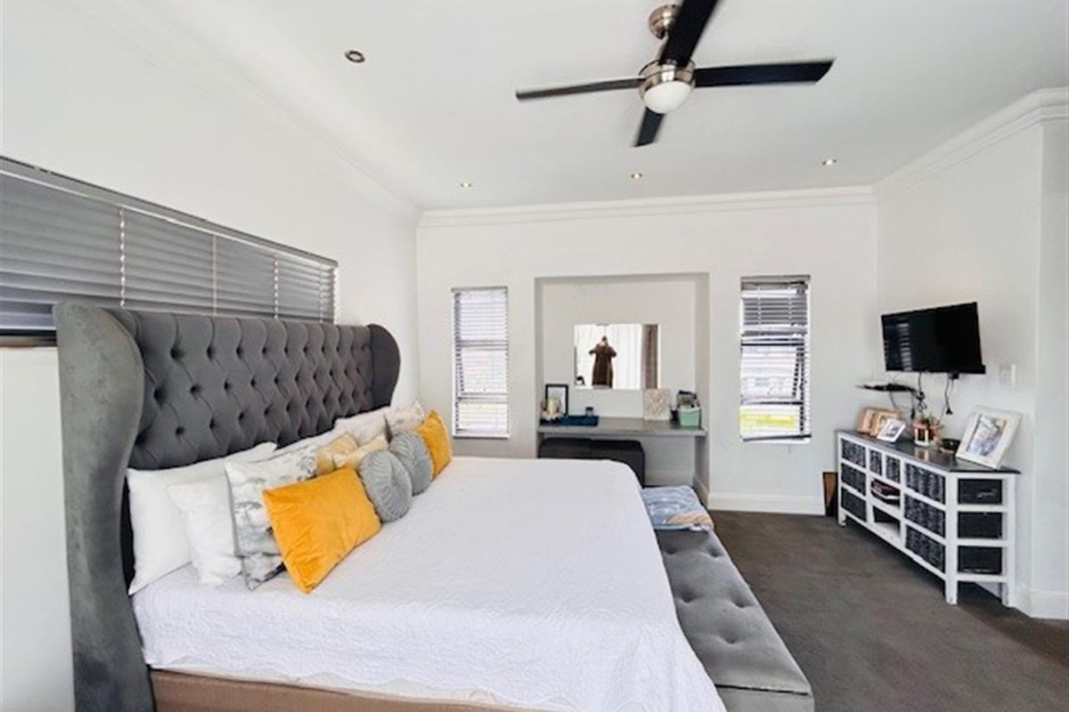 Spacious bedroom featuring a built-in vanity, recessed lighting, ceiling fan, and neutral finishes with crown molding.