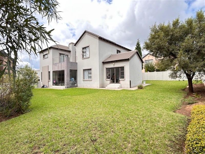 Rear view of a two-story residential house featuring a tiled roof, balcony, sliding glass doors, and a spacious private lawn.