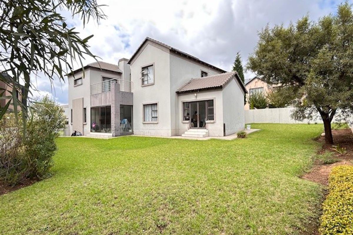 Rear view of a two-story residential house featuring a tiled roof, balcony, sliding glass doors, and a spacious private lawn.