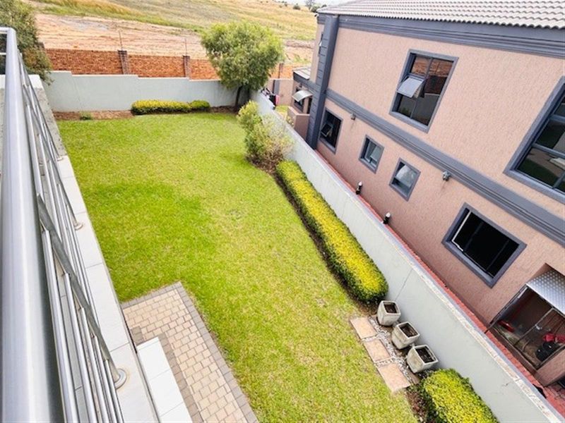 An elevated view of a private rear garden featuring a paved patio area, well-maintained lawn, and perimeter boundary wall.