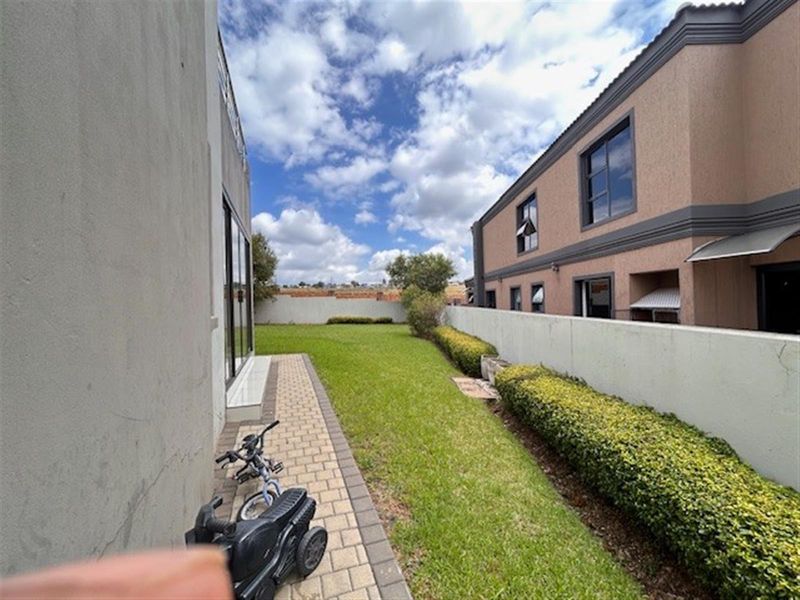 A rear garden area featuring a paved walkway, manicured lawn, and boundary wall, providing a private outdoor space adjacent to the main dwelling.