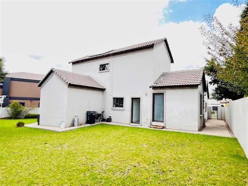 Rear view of the house featuring a tiled roof, paved side walkway, and a well-maintained lawn area.