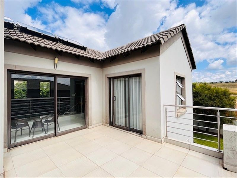 A spacious upper-level balcony featuring tiled flooring, stainless steel railings, and large sliding glass doors providing access to the interior.