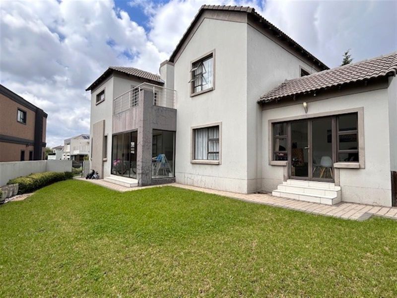 Rear view of a two-story residential house featuring a tiled roof, balcony, and paved patio area leading onto a private lawn.