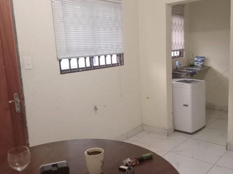 Open plan living area featuring tiled flooring and window blinds, with an adjacent utility or scullery space visible.