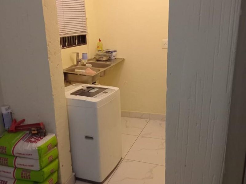 A functional laundry area featuring tiled flooring, a stainless steel sink, and a window with a venetian blind.