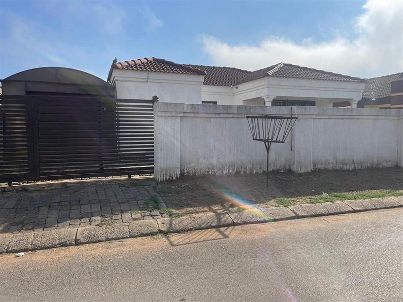 Front exterior view of the property featuring a perimeter wall, sliding gate, and tiled roof structure.
