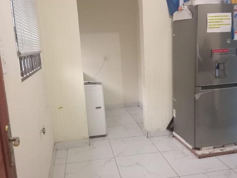 A functional scullery or utility area featuring tiled flooring and a window with venetian blinds, providing additional prep or storage space.