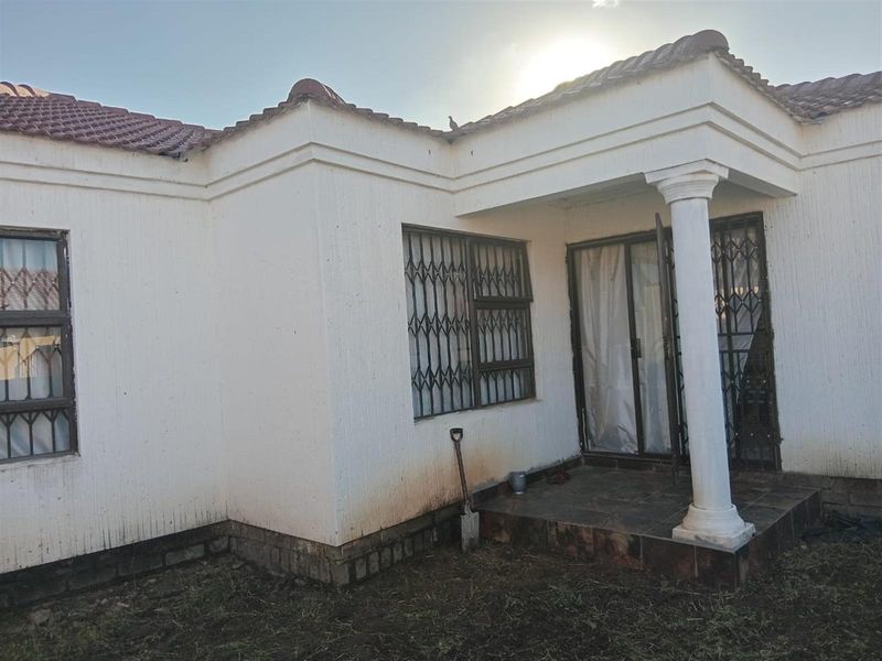 Rear exterior view of the house featuring a small tiled patio, security gates, and a covered entrance area with a decorative column.