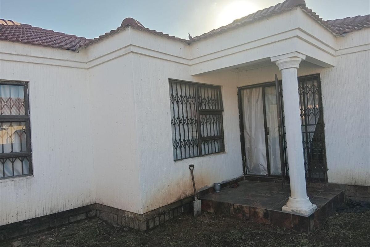 Rear exterior view of the house featuring a small tiled patio, security gates, and a covered entrance area with a decorative column.