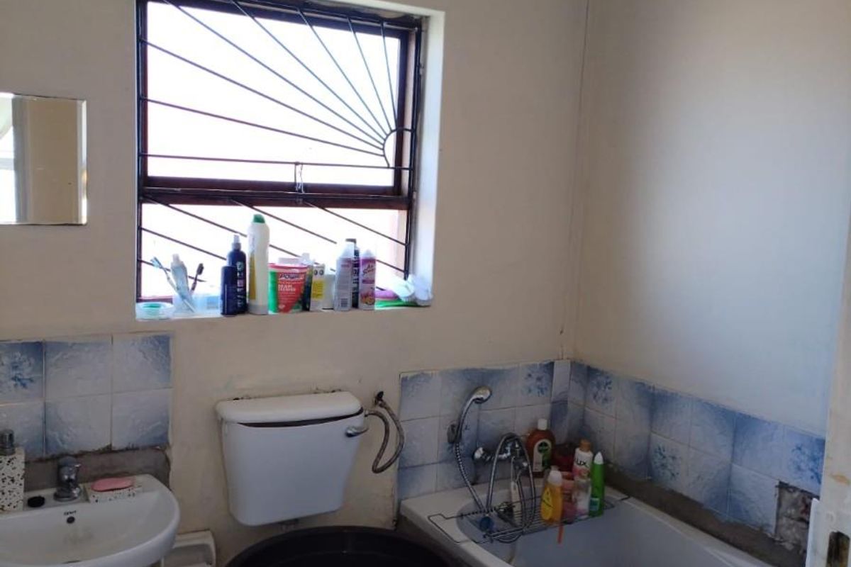 A dated bathroom featuring a standard bathtub, toilet, and wall-mounted basin, requiring renovation and cosmetic updates to improve its condition.