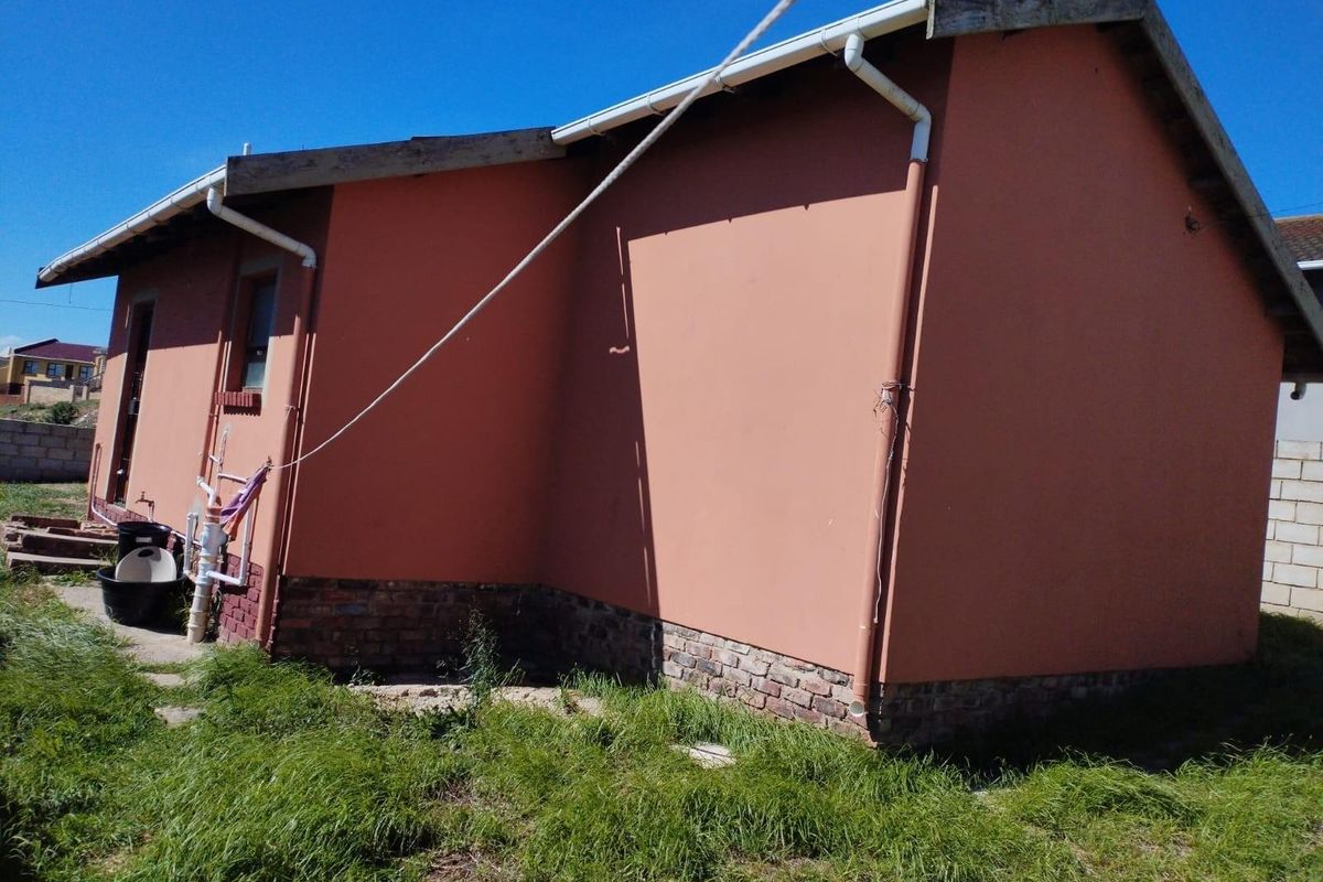 Rear exterior view of the house featuring a painted masonry facade, exposed plumbing, and guttering system set against a grassed backyard area.