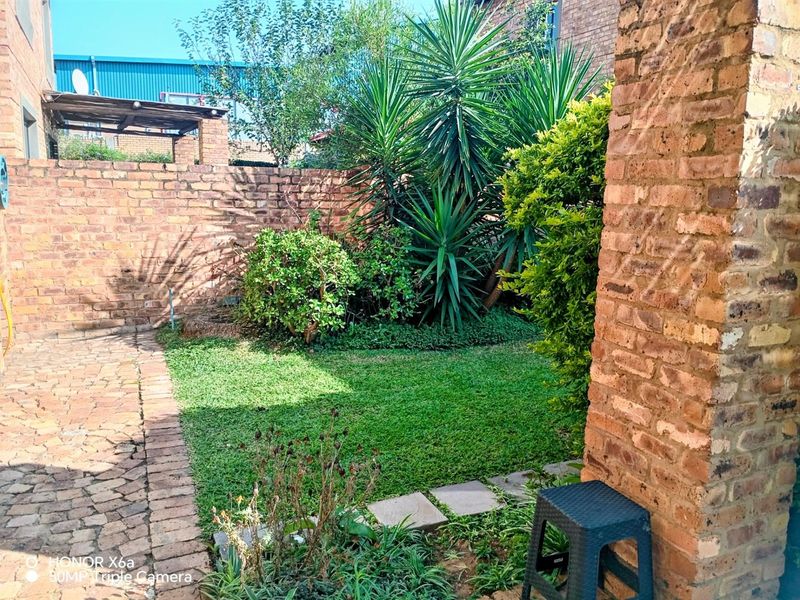 A private rear garden featuring a small lawn area, brick paving, and a rustic face-brick boundary wall.