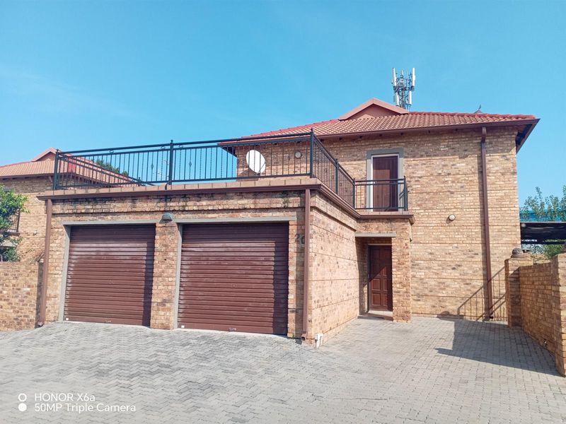 Front view of a double-story townhouse featuring a double garage, paved driveway, and an upper-level balcony with wrought iron railings.