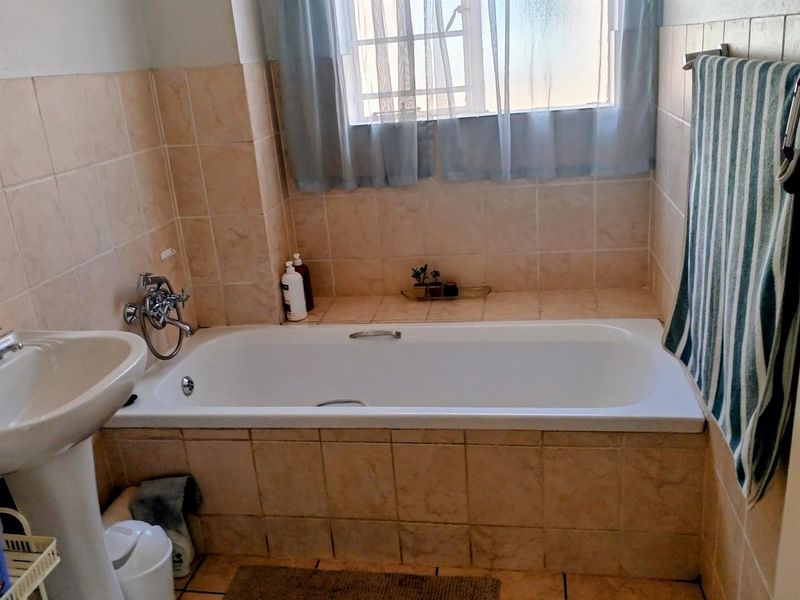 A functional bathroom featuring a built-in bathtub with chrome fixtures, a pedestal basin, and neutral ceramic wall and floor tiling.