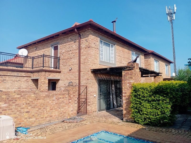 Rear exterior view of a face brick townhouse featuring a swimming pool, a balcony with iron railings, and a timber pergola over the patio area.