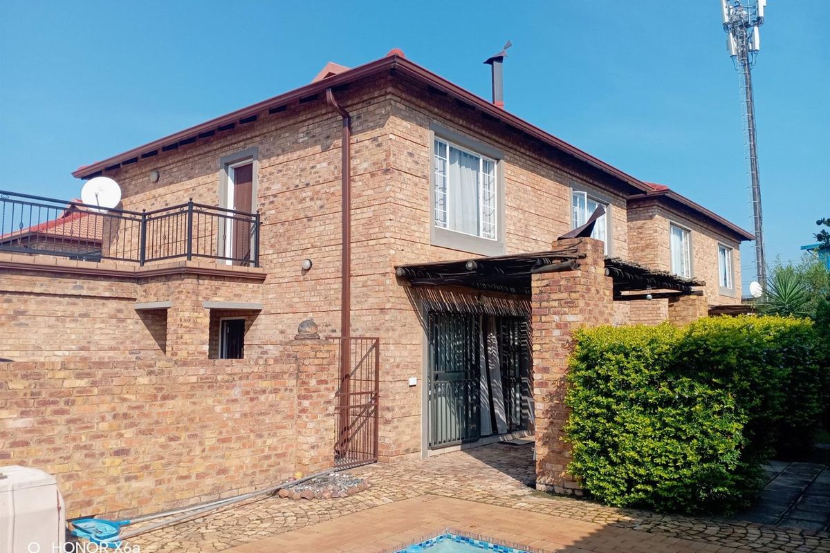 Rear exterior view of a face brick townhouse featuring a swimming pool, a balcony with iron railings, and a timber pergola over the patio area.
