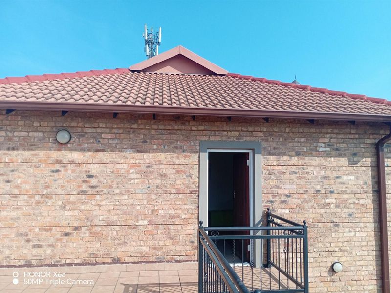 A balcony area featuring a brick facade, tiled flooring, and a wrought iron balustrade, providing access to the interior of the townhouse.